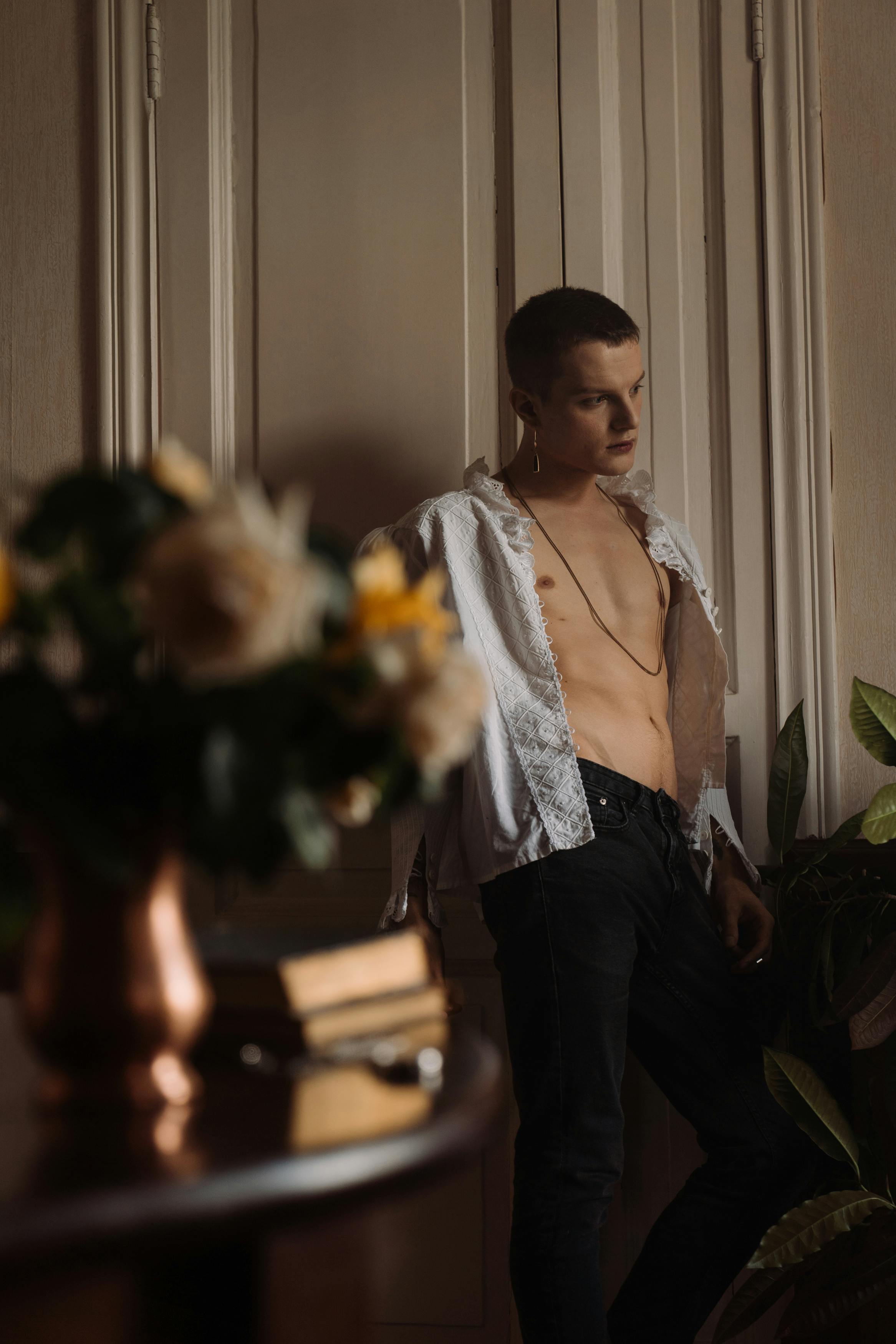 一名年轻人赤裸上身、穿着时尚的敞开衬衫，站在昏暗的灯光下