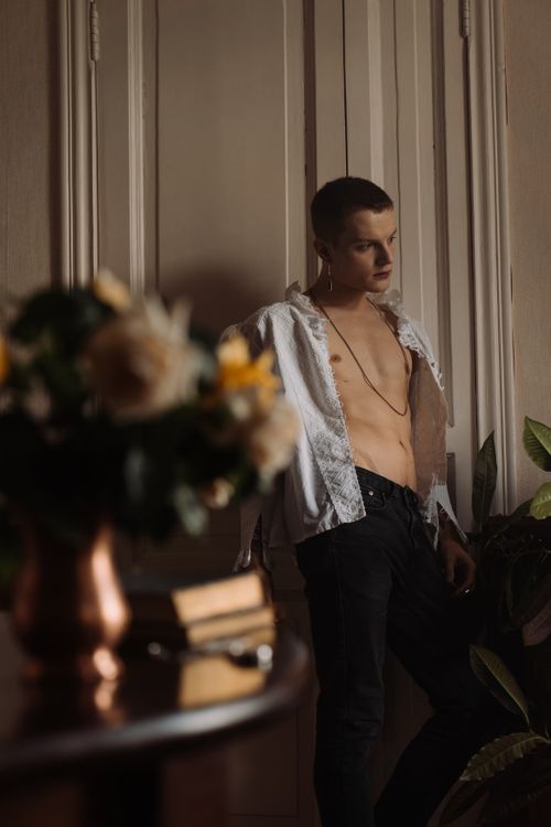 Free A shirtless young man with a stylish open shirt stands indoors in moody lighting. Stock Photo