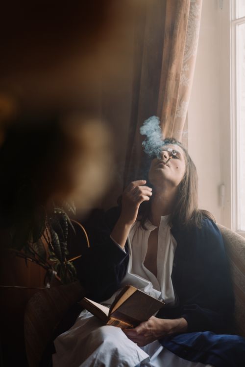Free Contemplative person smokes indoors while reading, soft light from window. Stock Photo