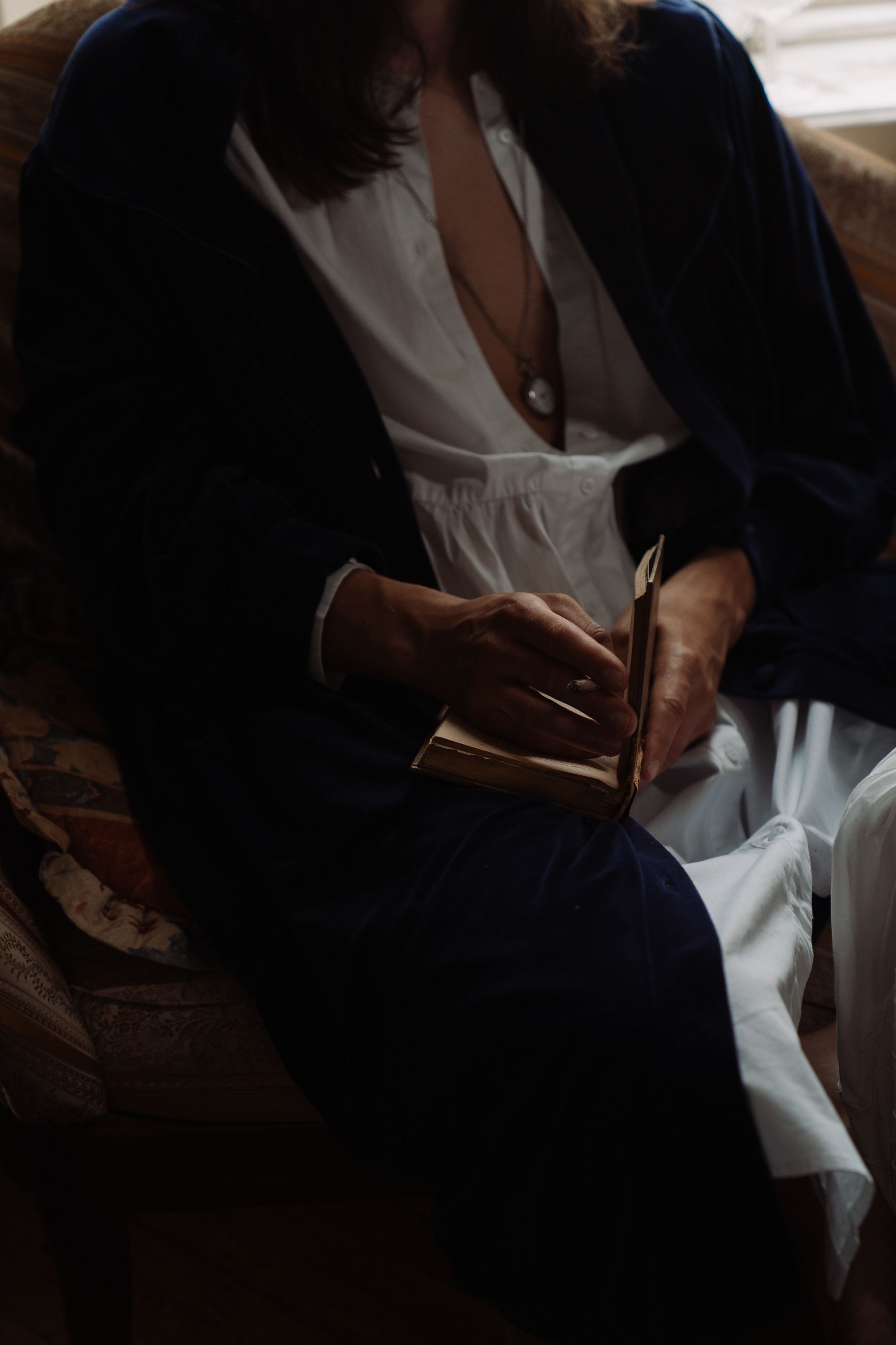 Pessoa em robe lendo um livro em ambientes internos com uma atmosfera calma e serena.