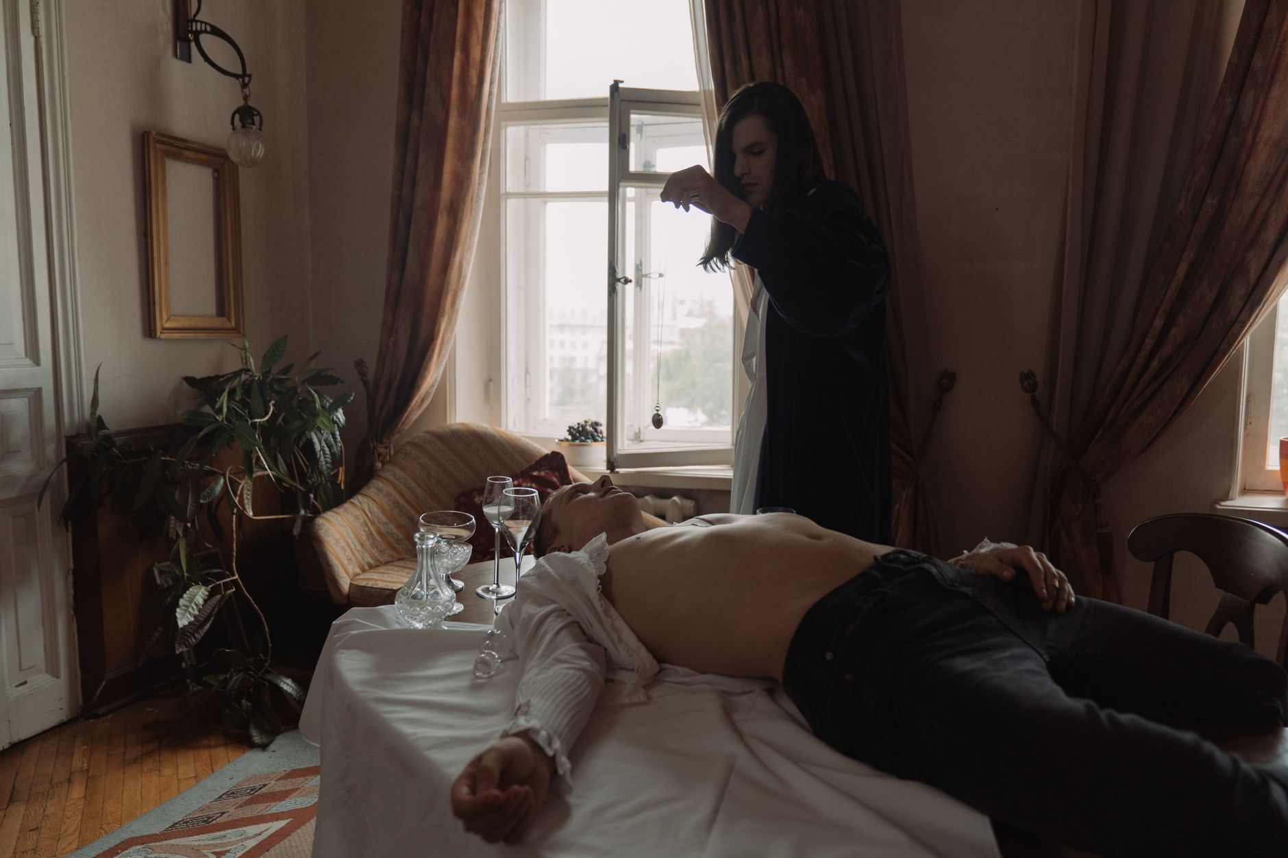 A mysterious androgynous figure performs a ritual in a vintage room, creating a dramatic atmosphere.