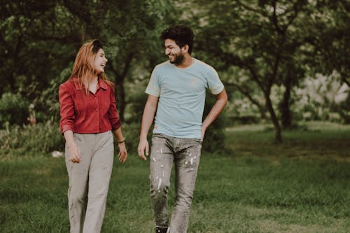 Free Positive young ethnic guy and lady in casual outfits laughing while having fun together in green park Stock Photo