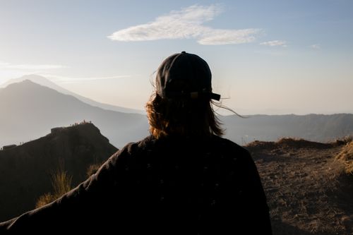 Free Back view of faceless tourist in casual clothing and hat looking at mountain range under light blue sky with clouds in daytime Stock Photo