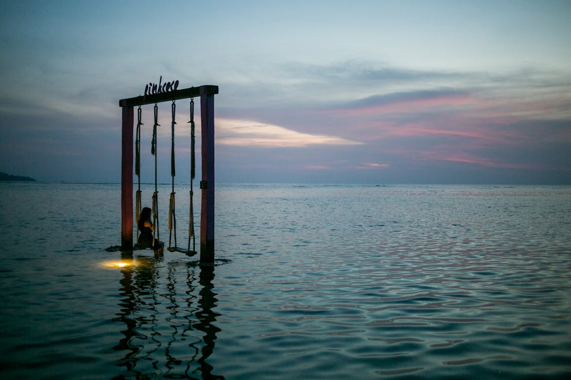 Faceless traveler on swing in sea at sunset