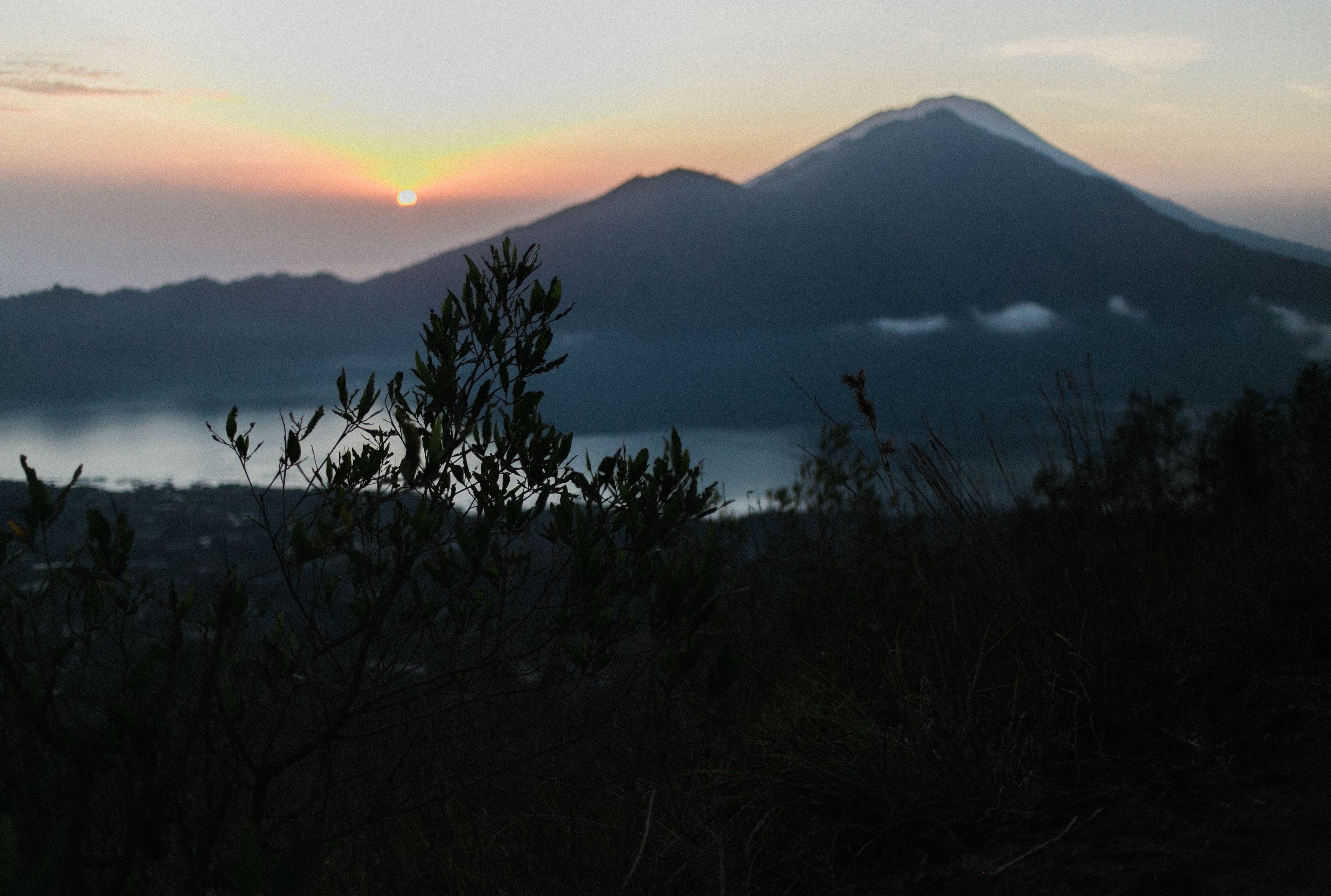 宁静的海岸线绿树成荫，平静的湖泊与朦胧的山脉在日落天空下相映成趣