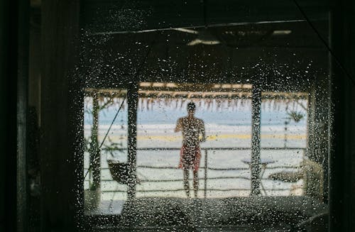 Free View through window in drops of man relaxing on terrace of exotic hotel against ocean Stock Photo