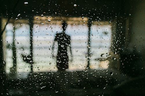 Silhouette of man behind window in wet raindrops standing on terrace of resort