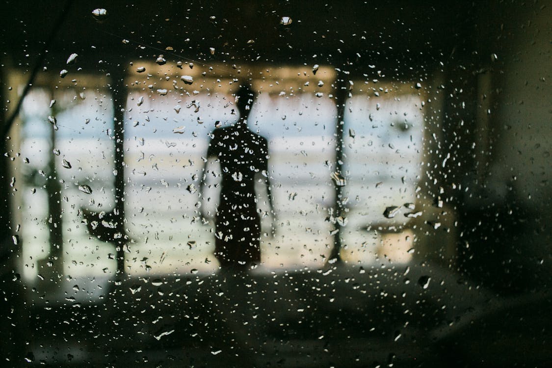 Free Silhouette of man behind window in wet raindrops standing on terrace of resort Stock Photo