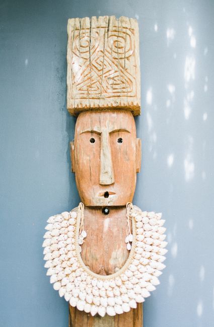 Ornamental exotic figure of pagan god with carved ornaments and in necklace against white wall