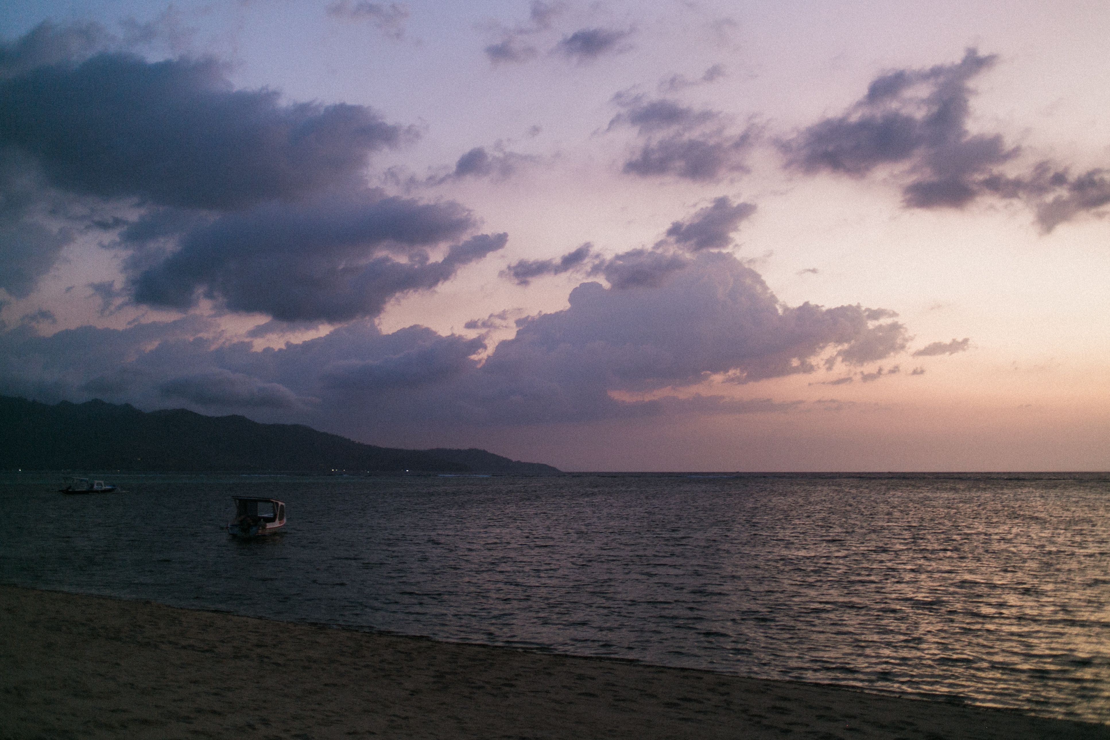 宁静的海岸线，波光粼粼的海水，以及日落时云下漂浮的小舟