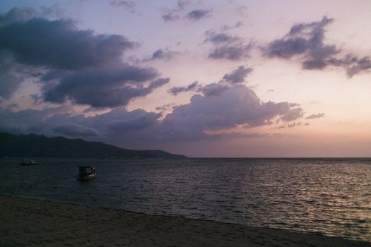 宁静的海岸线，波光粼粼的海水，以及日落时云下漂浮的小舟