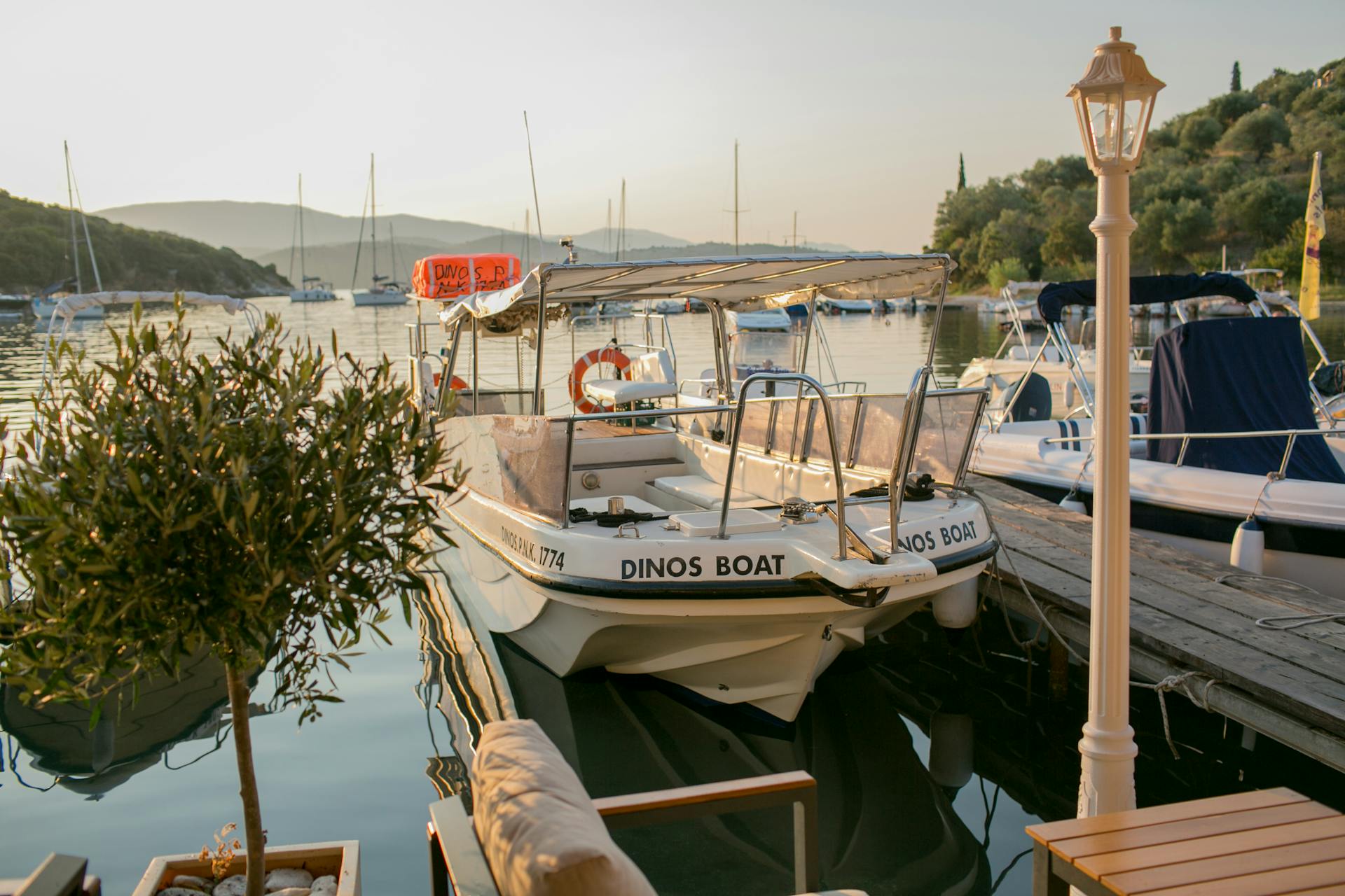Tranquil marina scene with boats docked at sunset, surrounded by nature.