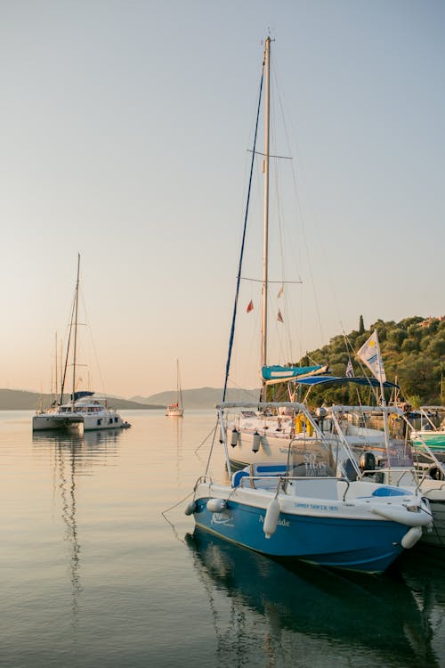 Moored boats floating on tranquil water of sea lagoon with green hills in dusky time