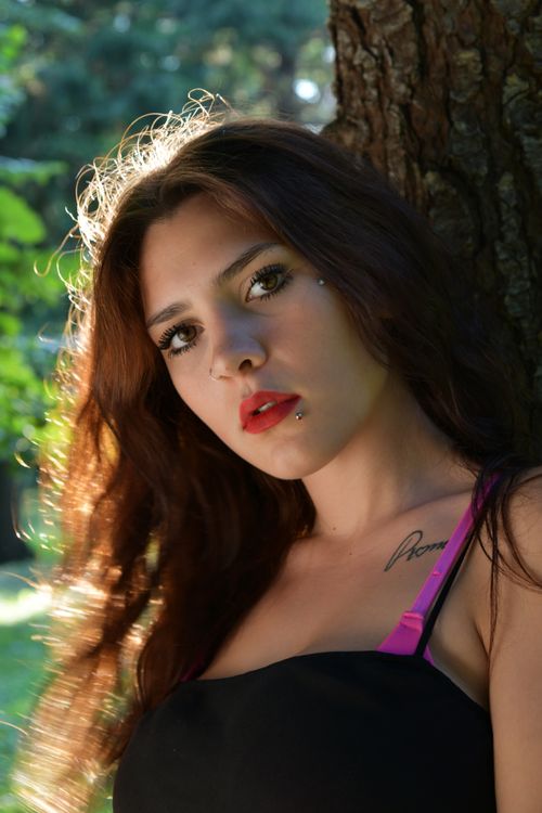 Free Portrait of a young woman with red lips and piercings, outdoors in sunlight. Stock Photo