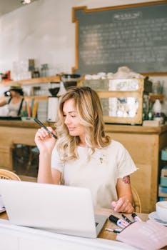 Woman working on laptop in a bright café, embodying remote work and freelancer lifestyle.