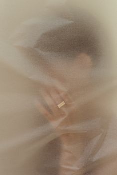 一幅风格柔和的抽象肖像中，一只手正透过半透明材料佩戴戒指
