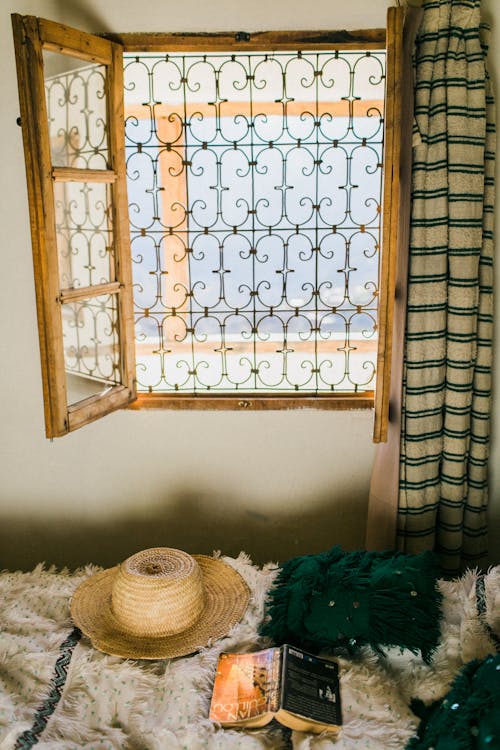 Interior of room with oriental bars on window and straw hat with book on bed below