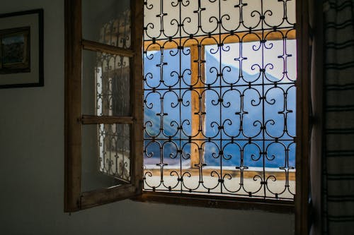 Opened window with bars viewing majestic mountains and terrace in bright summer sunlight