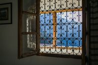 Opened window with bars viewing majestic mountains and terrace in bright summer sunlight