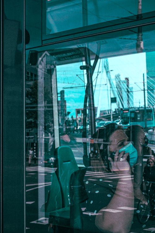 Free Woman on phone with mask reflected in bus window, Erasmus Bridge view. Stock Photo