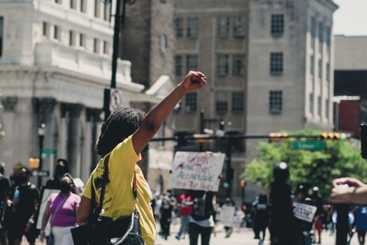 African American female raising fist while standing in demonstration against police brutality in daylight