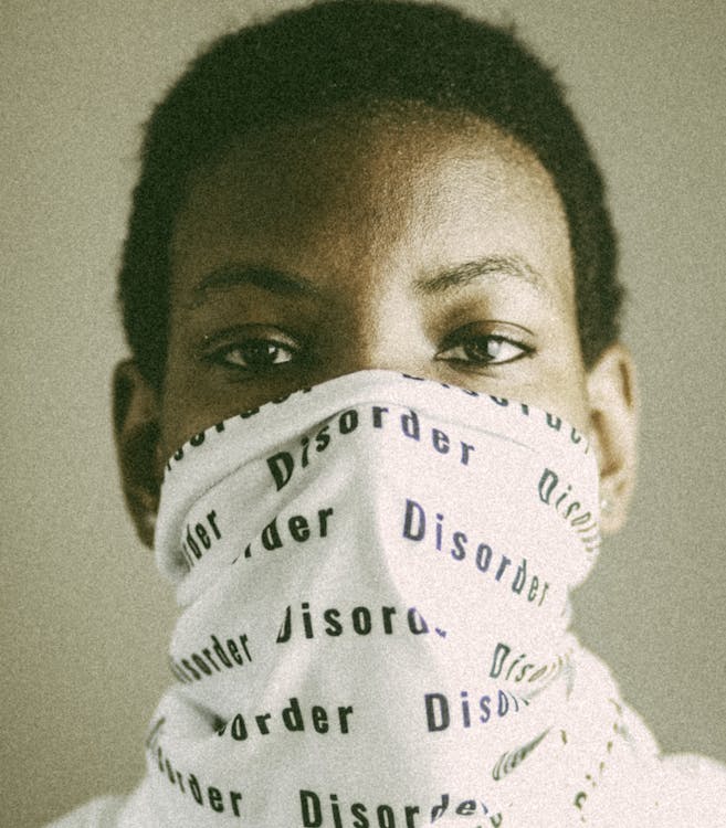Pensive African American person with short black hair in white balaclava with inscription Disorder on surface looking at camera on black background