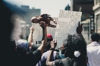 Faceless protesters in casual clothing and fabric masks showing sheets with slogans and black doll on picket in daytime