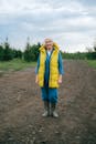 一位穿着黄色背心和橡胶靴的老妇人走在土路上，展现了农村生活的场景