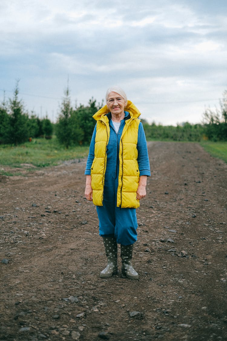 Woman In Yellow Vest Standing On Dirt Road