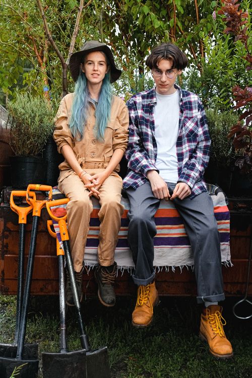 Free A teenage couple sitting on a wooden bench surrounded by plants and gardening tools. Stock Photo