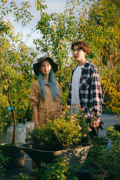 Free Two young gardeners standing in a lush garden with vibrant plants and trees. Stock Photo