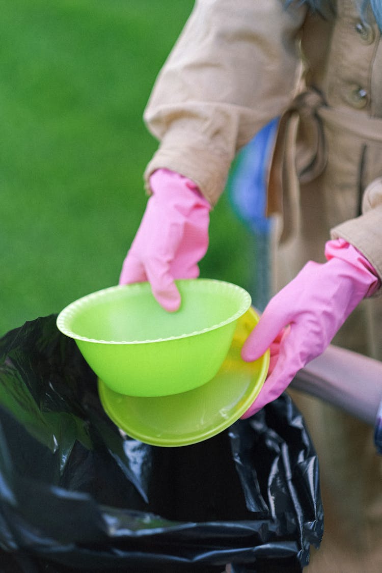 

A Close-Up Shot Of A Person Wearing Gloves Throwing Plastic Food Containers In A Garbage Bag