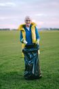 An Elderly Woman Putting Trash Inside Black Plastic Bag while Seriously Looking at the Camera