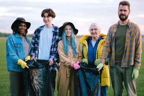 Free Group of smiling volunteers cleaning a green field, holding plastic bags. Diverse team promoting environmental care. Stock Photo