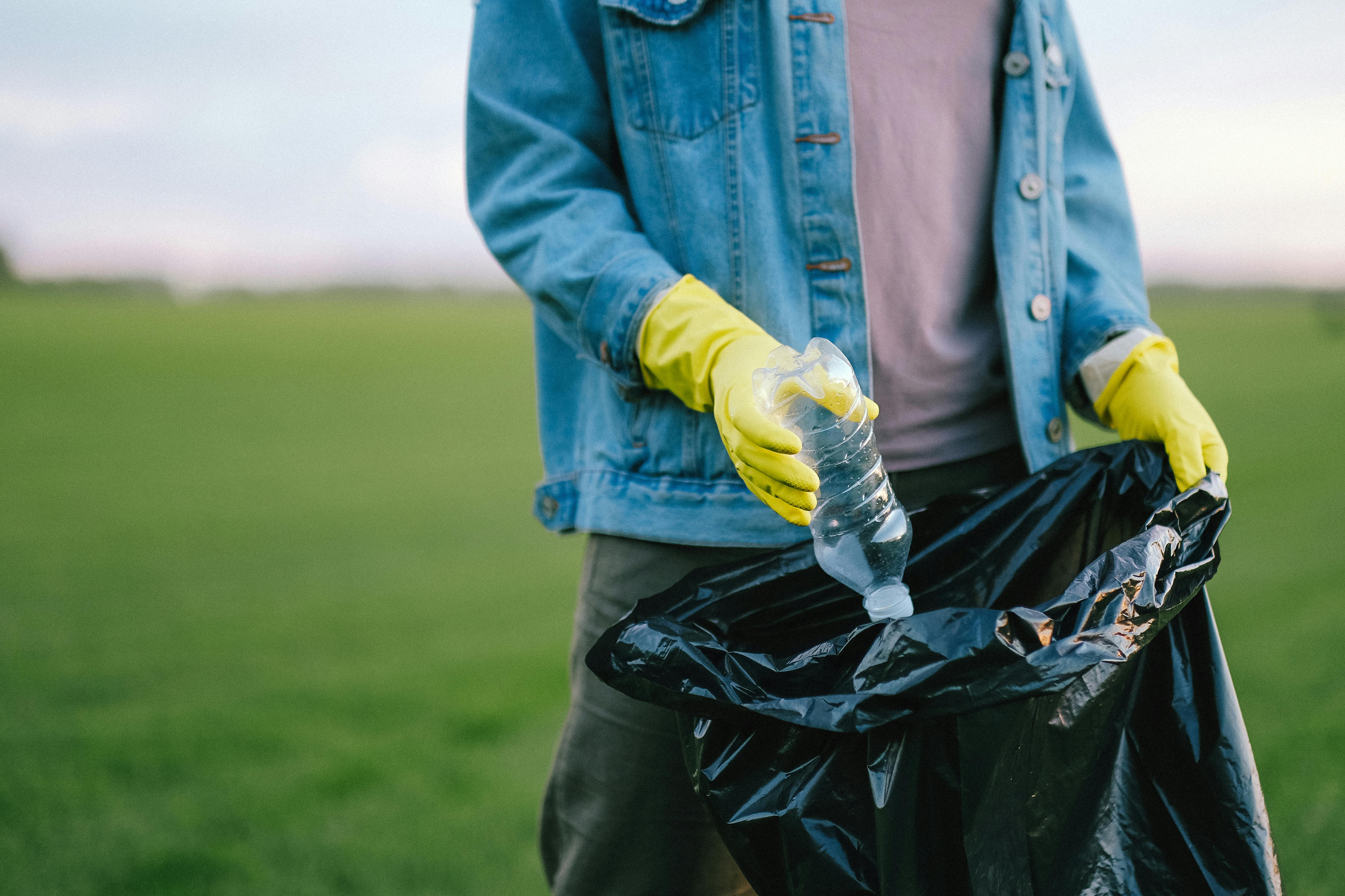 person in blue denim jacket putting plastic bottle inside black garbage bag