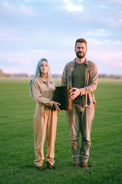 A Man and a Woman Standing on Grass Field while Holding Black Plastic Pot