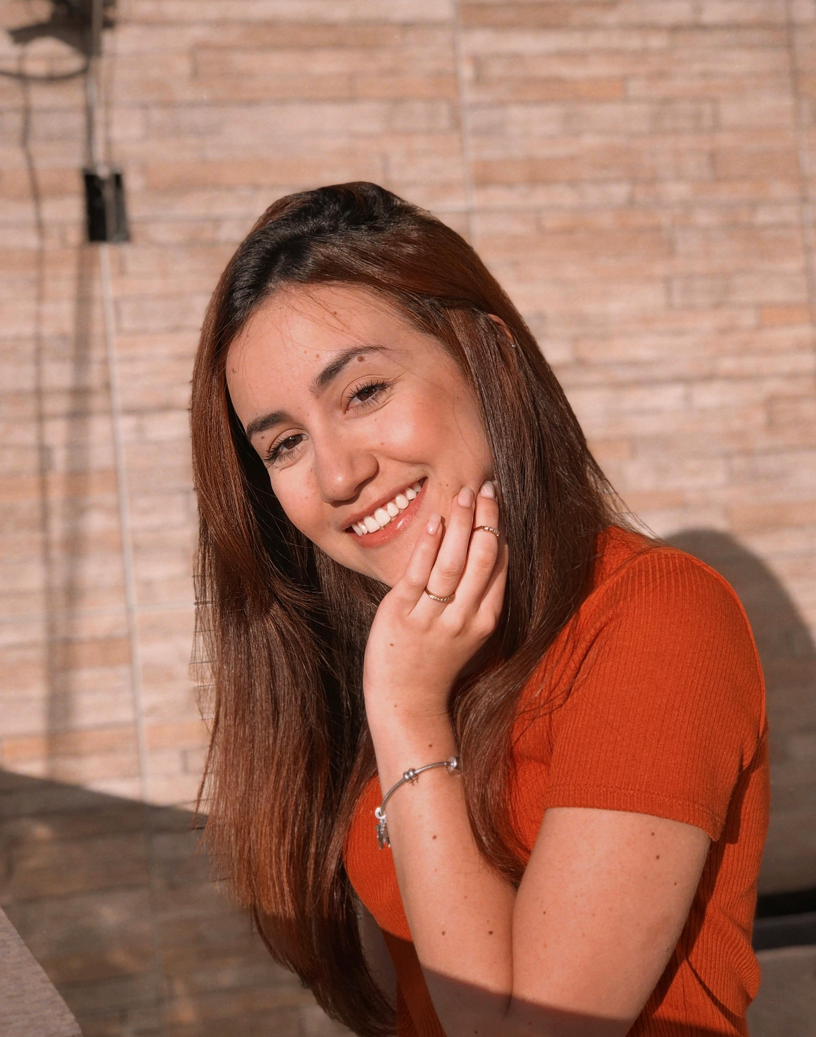 Bright outdoor portrait of a smiling woman in an orange shirt, capturing warmth and positivity.