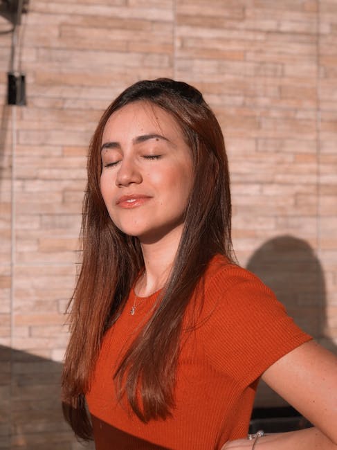 Natural light portrait of a woman in an orange shirt against a brick wall, enjoying the sun.