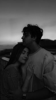 A young couple embraces tenderly in a grayscale twilight setting.