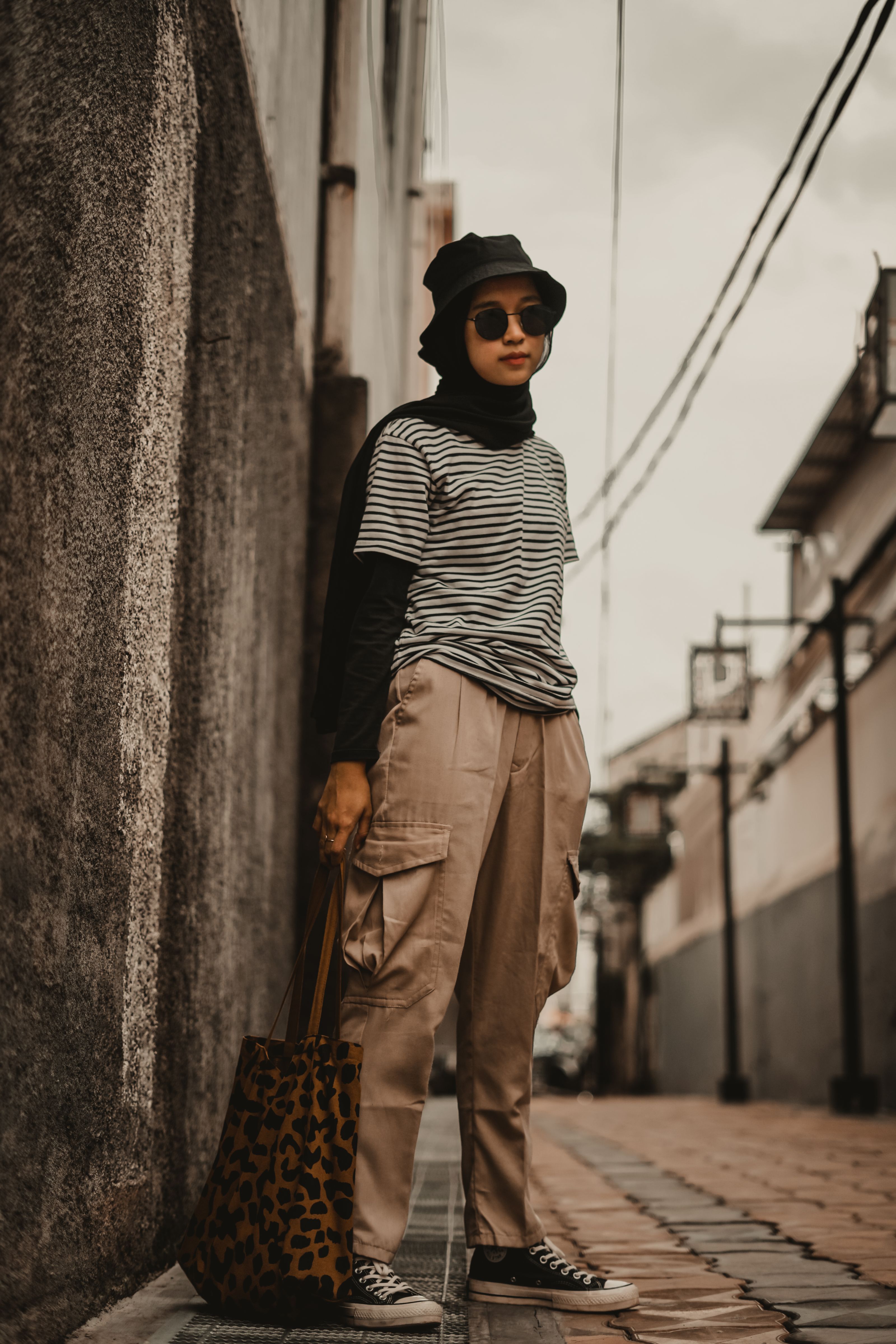 Mulher estilosa em ambiente urbano com chapéu de balde e bolsa de estampa de leopardo, exibindo moda de rua.