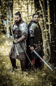 Two armored warriors in a forest setting, ready for battle with weapons in hand.