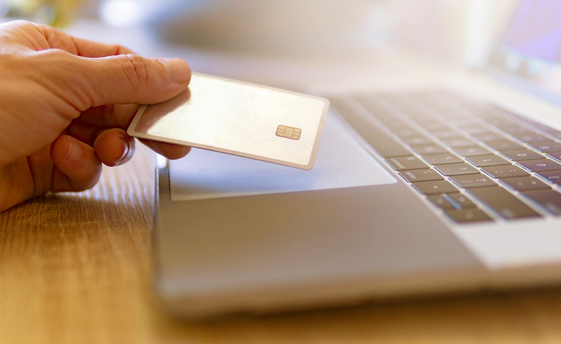 A person holds a credit card near a laptop for online shopping.