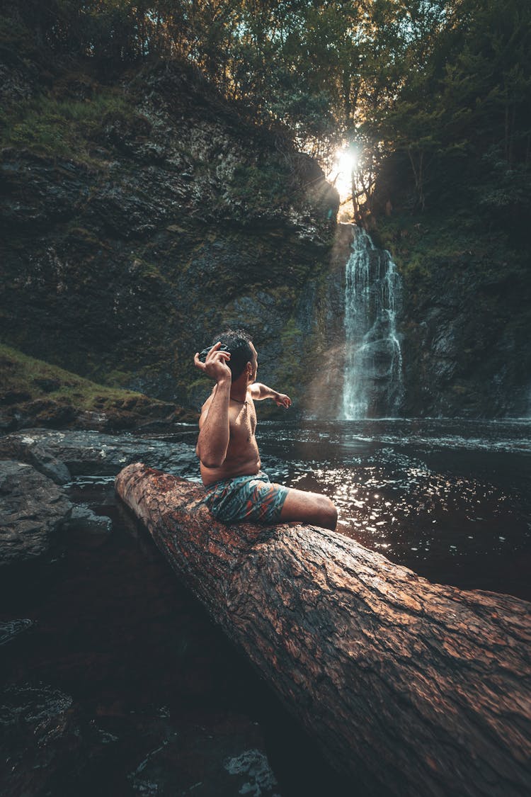 Photo Of A Man Sitting On A Log While Throwing A Rock