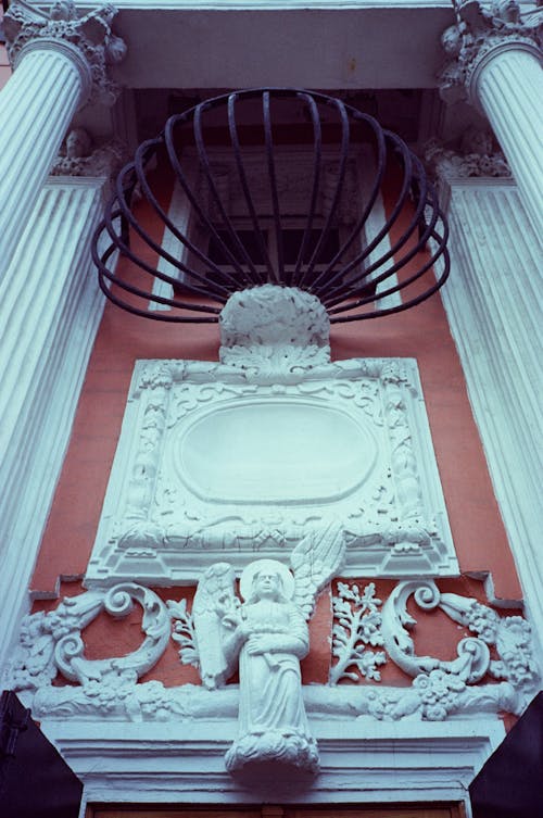 From below of bas relief and sculptures decorating facade of aged building with columns in daytime