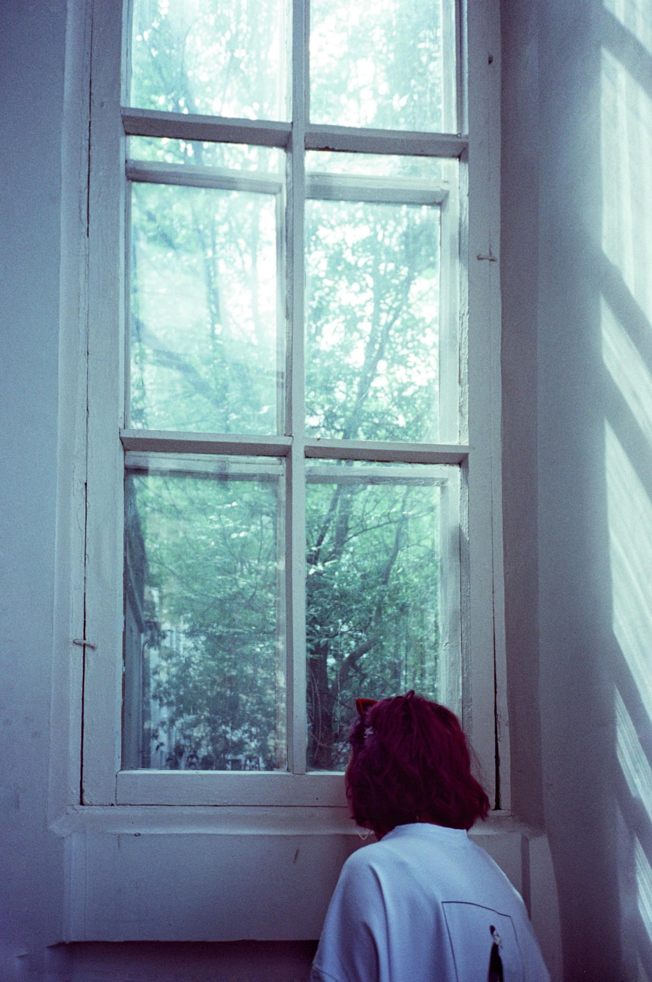 Anonymous woman standing near window overlooking forest · Free