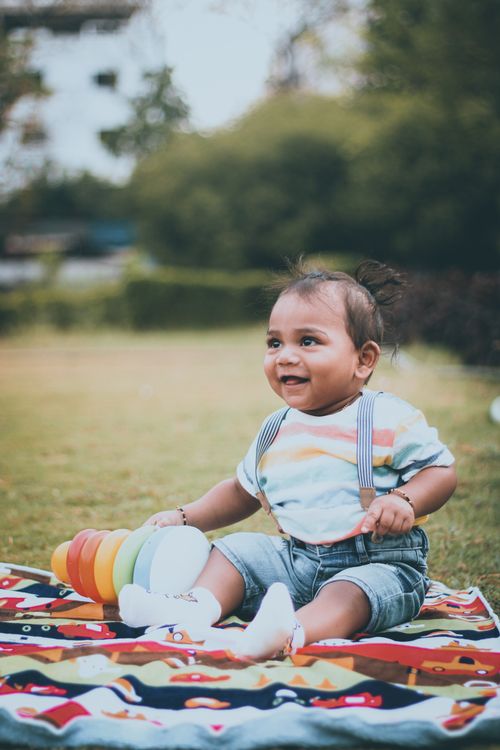 Free Adorable baby sitting on a colorful blanket outdoors with toys and smiling cheerfully. Stock Photo