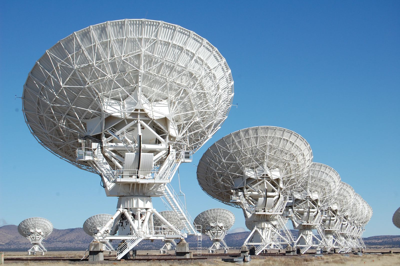 Row of large white radio telescope dishes standing in an open desert landscape