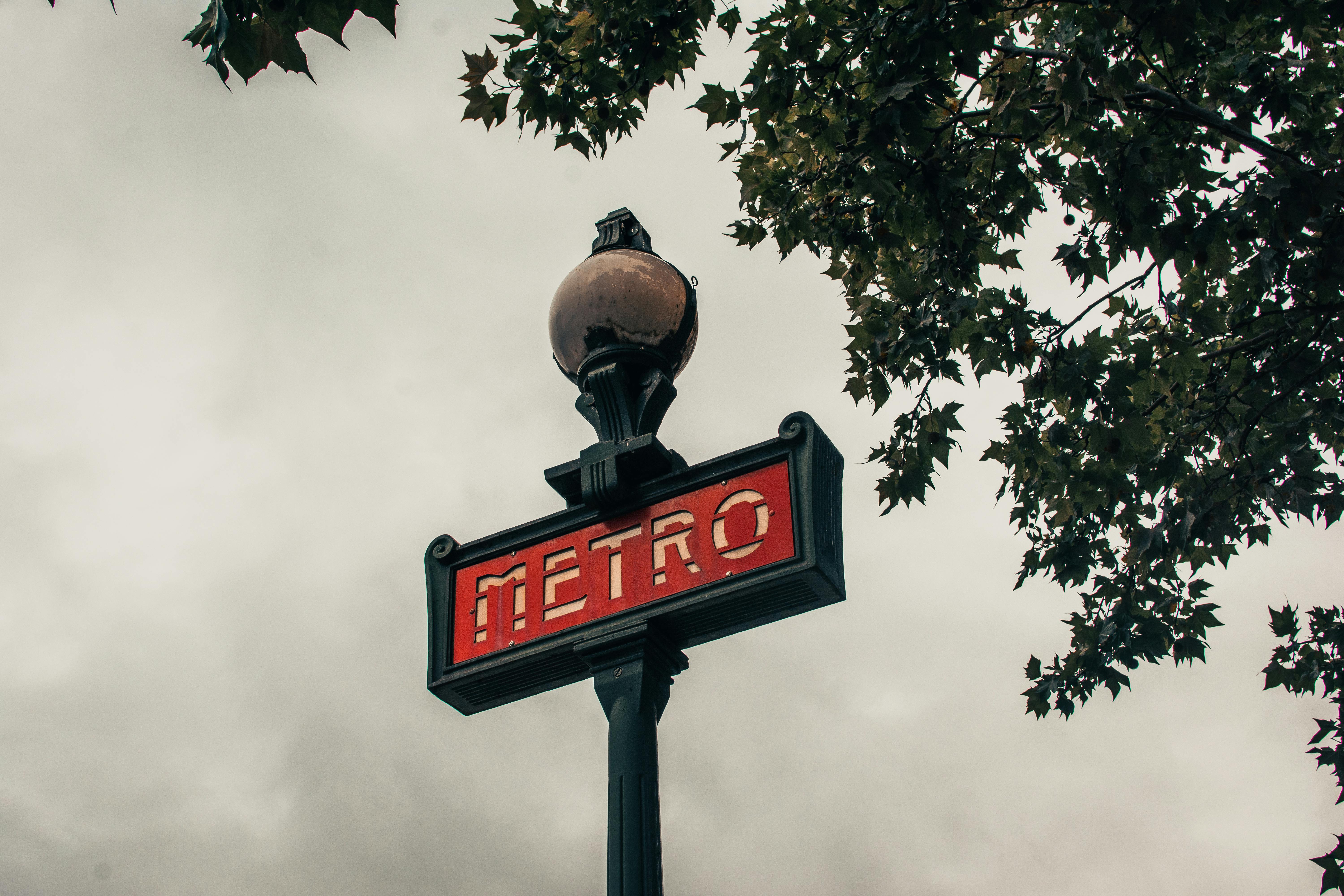 Iconic Paris Metro sign under a cloudy sky with tree leaves framing the scene.