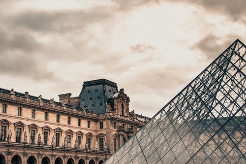 Free The Louvre Museum's historic facade with its iconic glass pyramid on a cloudy Parisian day. Stock Photo