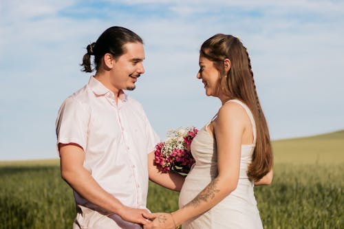 Man in Button Up Shirt Holding Bouquet of Flowers Beside Woman in White Sleeveless Dress